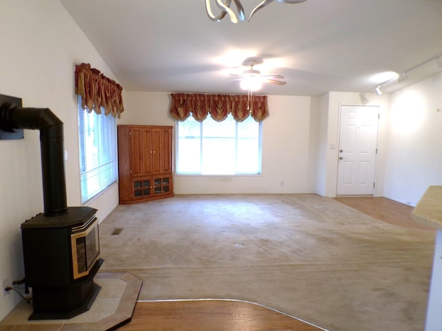 unfurnished living room with ceiling fan, a wood stove, light carpet, and track lighting