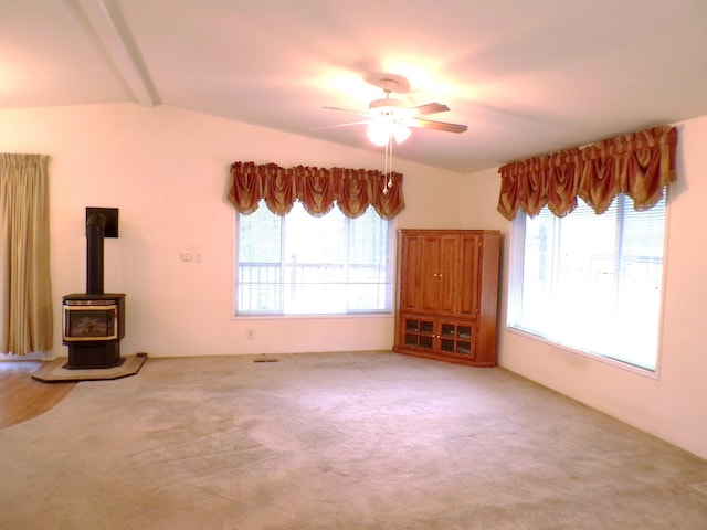 unfurnished living room featuring ceiling fan, carpet, vaulted ceiling with beams, and a wood stove