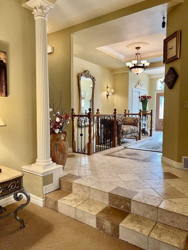 hall with a notable chandelier, ornate columns, ornamental molding, and a tray ceiling