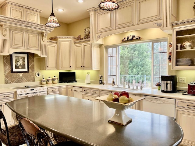 kitchen with white appliances, hanging light fixtures, cream cabinetry, sink, and a breakfast bar area