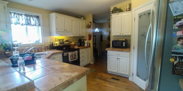 kitchen with sink, hardwood / wood-style floors, stainless steel appliances, tile counters, and white cabinets