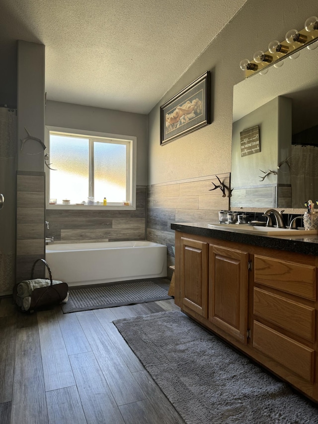 bathroom with a tub to relax in, wood-type flooring, a textured ceiling, tile walls, and vanity