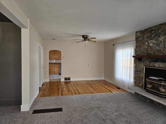 unfurnished living room featuring ceiling fan, a stone fireplace, and carpet flooring