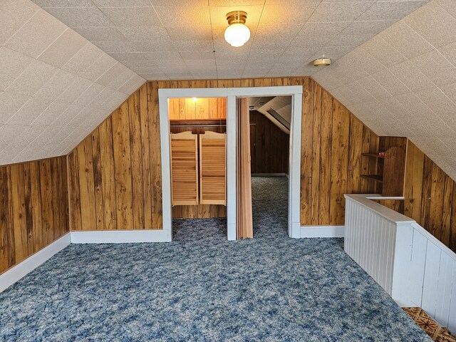 additional living space featuring wood walls, dark colored carpet, and lofted ceiling