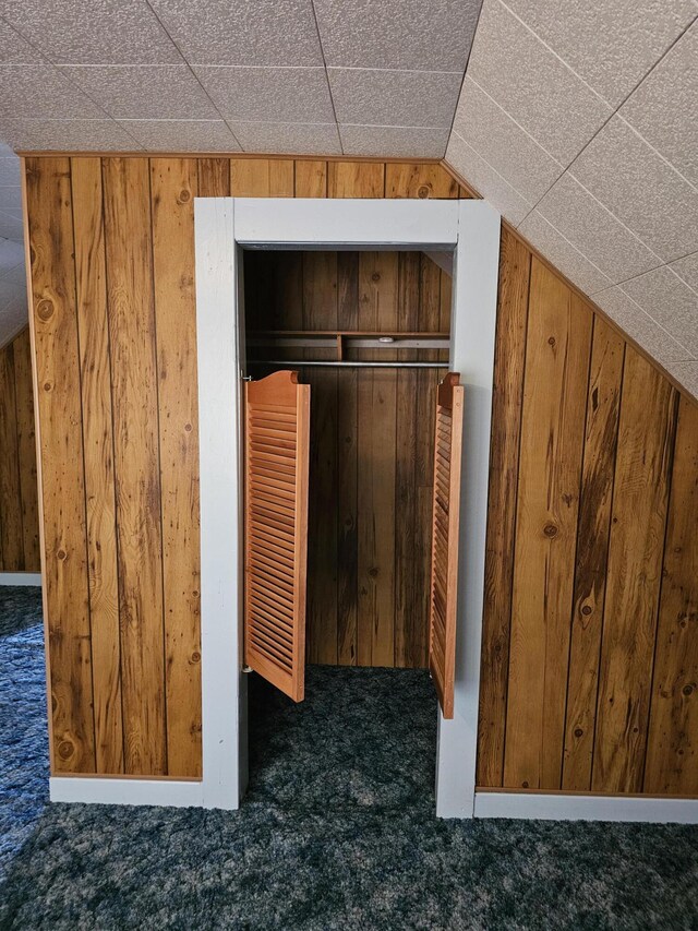 interior space featuring wood walls, vaulted ceiling, and dark carpet