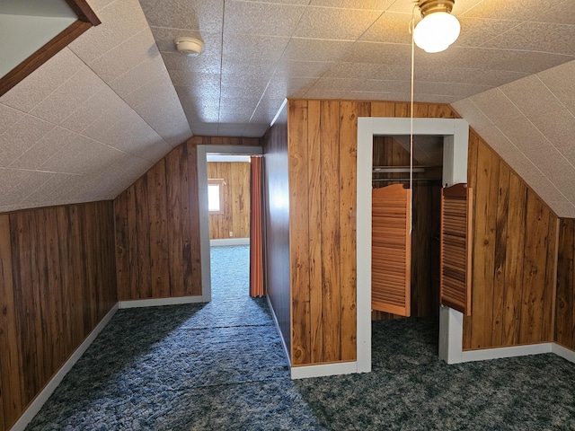 bonus room featuring dark colored carpet, wooden walls, and vaulted ceiling