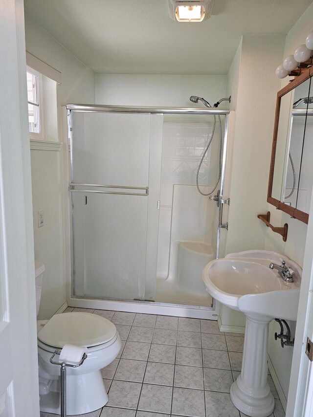 bathroom featuring a shower with door, toilet, and tile patterned flooring