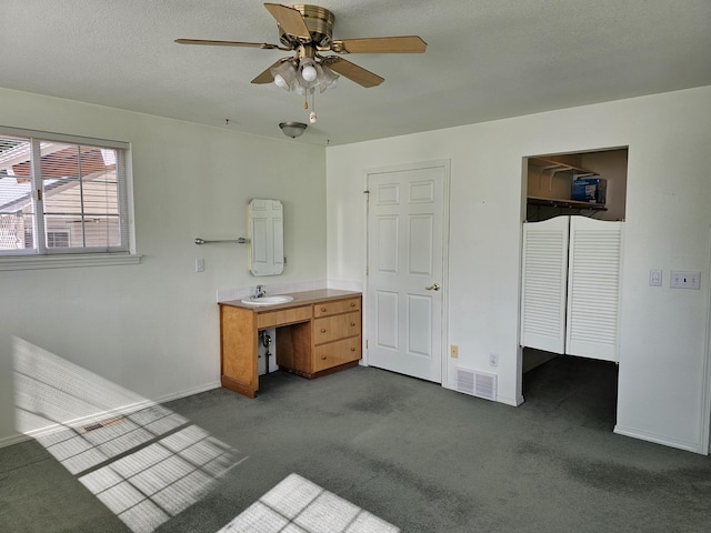 unfurnished bedroom with sink, ceiling fan, dark colored carpet, and a closet