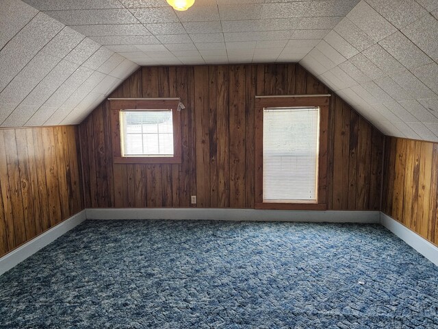 additional living space featuring wood walls, lofted ceiling, and carpet flooring