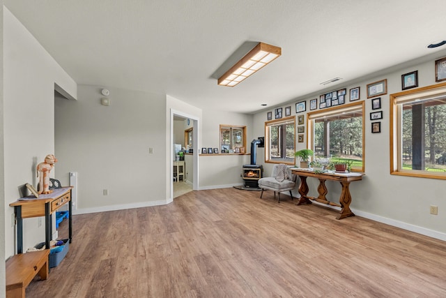 sitting room featuring visible vents, a wood stove, wood finished floors, and baseboards