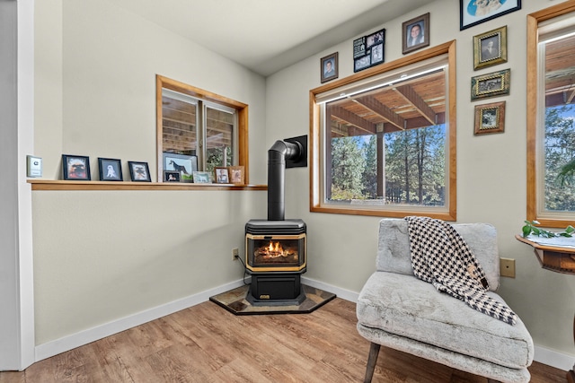 sitting room with a wood stove, baseboards, and wood finished floors