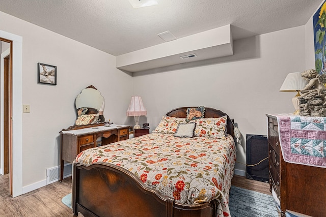 bedroom featuring visible vents, baseboards, wood finished floors, and a textured ceiling