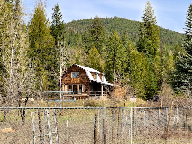 view of front of house with fence, a gambrel roof, a view of trees, and an outbuilding
