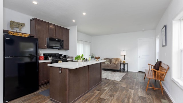 kitchen featuring an island with sink, a kitchen breakfast bar, dark hardwood / wood-style flooring, dark brown cabinetry, and black appliances