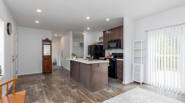 kitchen featuring an island with sink, dark brown cabinets, dark hardwood / wood-style floors, and black appliances