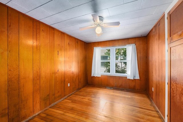 spare room with ceiling fan, light hardwood / wood-style flooring, and wooden walls