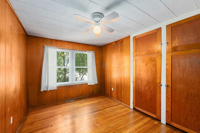 unfurnished bedroom featuring ceiling fan, wooden walls, and multiple closets