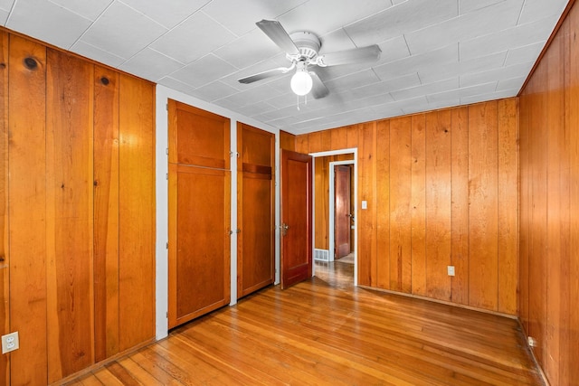 unfurnished bedroom with light wood-type flooring, wooden walls, and ceiling fan