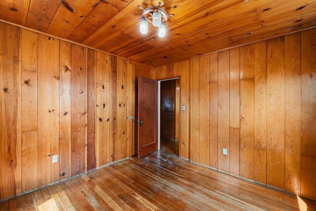 empty room featuring ceiling fan, hardwood / wood-style floors, and wooden walls