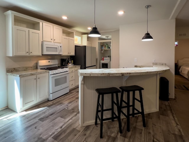 kitchen featuring dark wood-style floors, a breakfast bar, white appliances, white cabinets, and visible vents