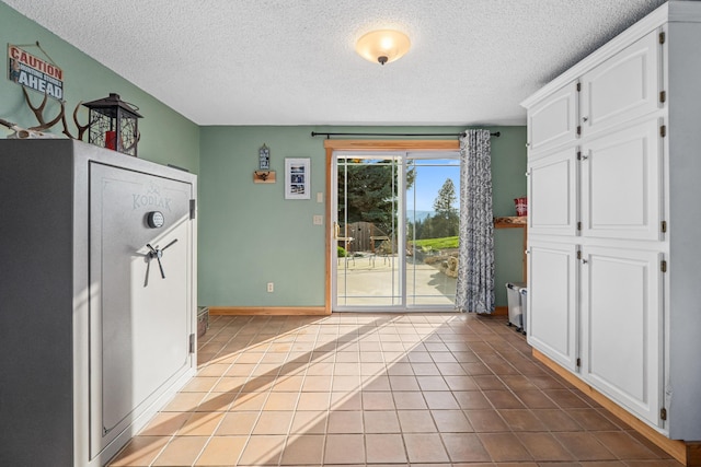 doorway to outside with baseboards, a textured ceiling, and tile patterned floors
