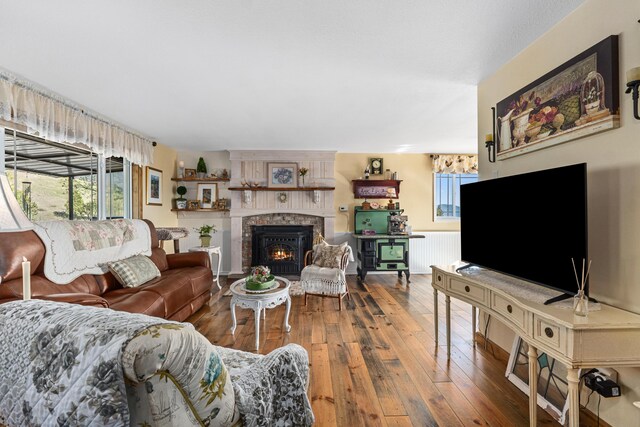 living area with wood-type flooring, radiator, a wealth of natural light, and a lit fireplace