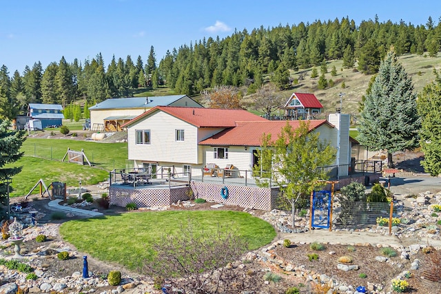 rear view of property featuring a lawn, a tile roof, a deck, and a forest view
