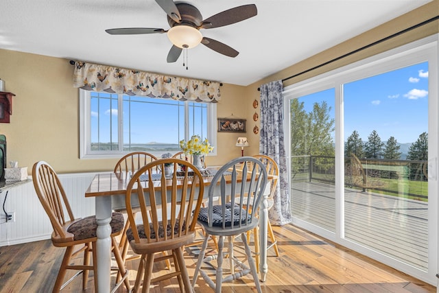 dining room with a healthy amount of sunlight, ceiling fan, wood-type flooring, and wainscoting