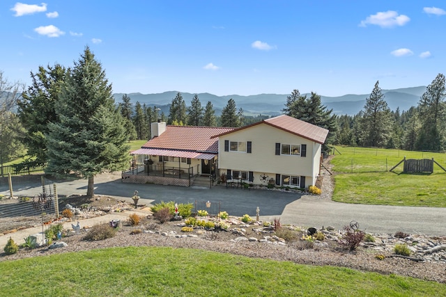 back of house with a lawn, a mountain view, a chimney, and fence