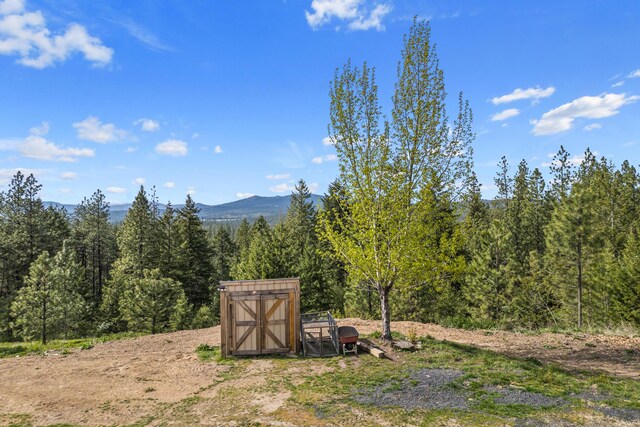 view of yard with a forest view, a mountain view, an outdoor structure, and a storage unit