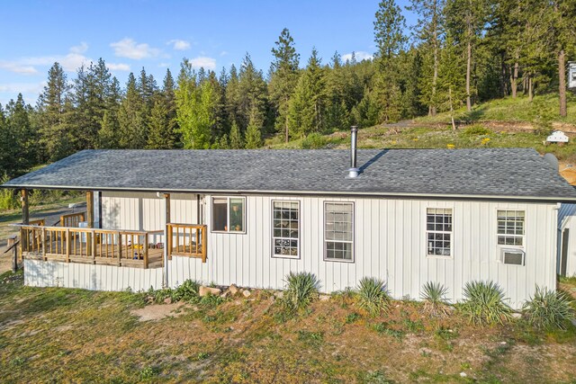exterior space featuring a wooded view, a shingled roof, board and batten siding, and a deck