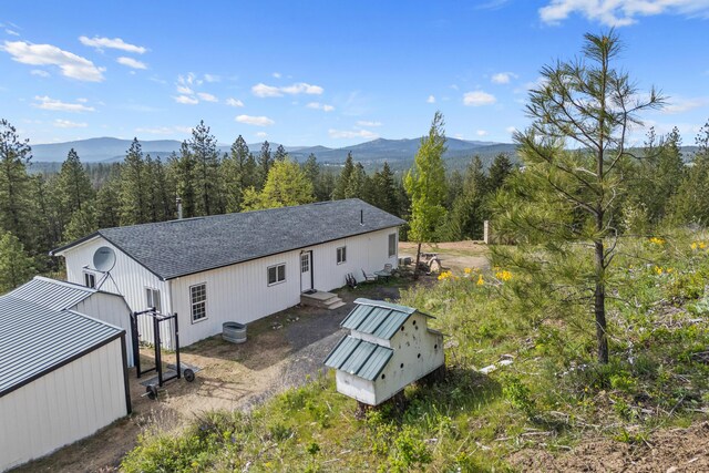 rear view of property featuring a shingled roof, a mountain view, and a forest view