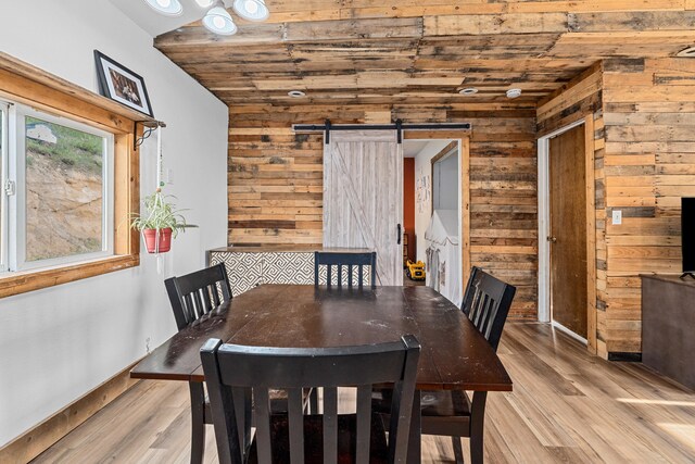 dining area with wood ceiling, wood walls, a barn door, baseboards, and light wood-style flooring