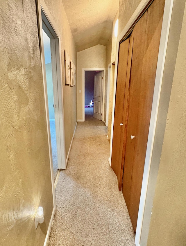 hallway featuring a textured ceiling, light colored carpet, and vaulted ceiling