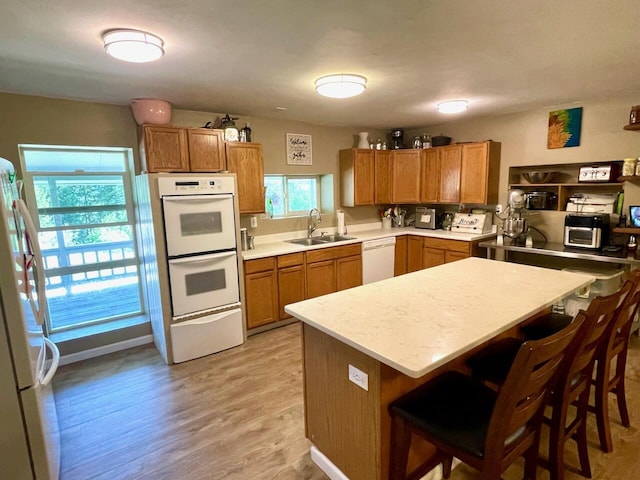 kitchen featuring kitchen peninsula, sink, light wood-type flooring, white appliances, and a breakfast bar area