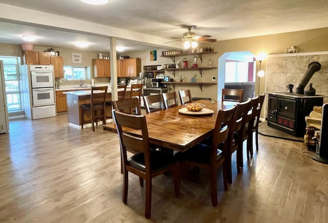 dining room with sink, light hardwood / wood-style floors, ceiling fan, and a wood stove