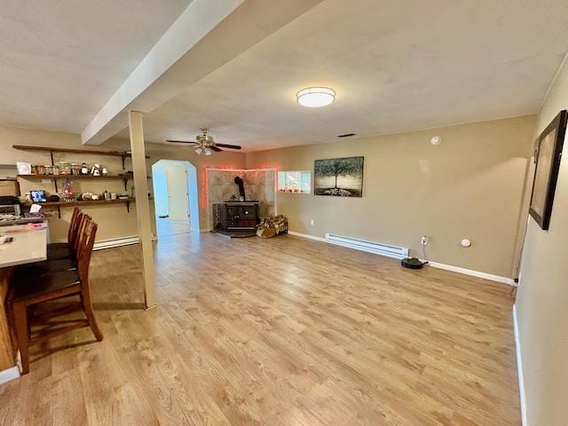 interior space featuring light wood-type flooring, a wood stove, ceiling fan, and a baseboard heating unit