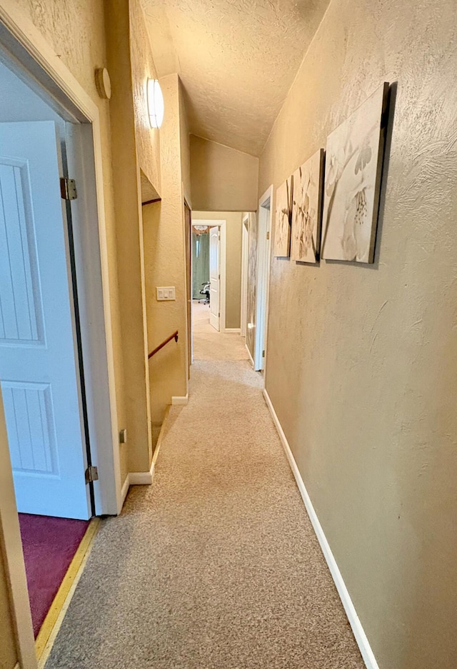 hallway featuring a textured ceiling, carpet, and vaulted ceiling