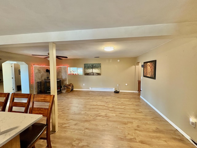 dining space featuring a wood stove, ceiling fan, a baseboard radiator, and hardwood / wood-style flooring