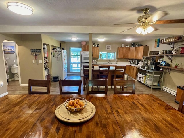 dining space featuring ceiling fan, sink, a baseboard heating unit, and dark hardwood / wood-style flooring