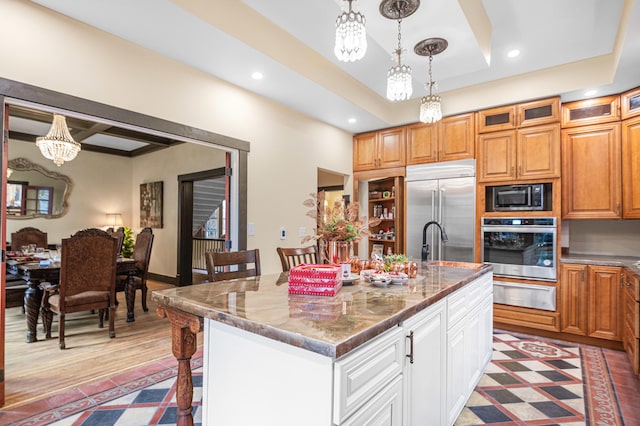 kitchen featuring hanging light fixtures, white cabinets, a kitchen bar, a kitchen island with sink, and built in appliances