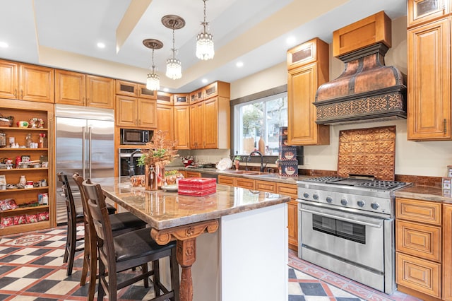 kitchen with premium appliances, custom exhaust hood, sink, a tray ceiling, and a kitchen island