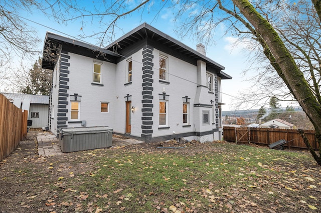 rear view of property with a hot tub and a yard