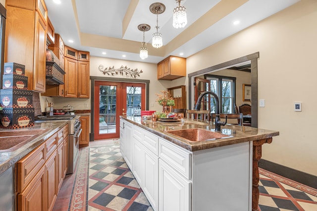 kitchen with french doors, white cabinetry, a tray ceiling, high end stainless steel range oven, and a center island with sink