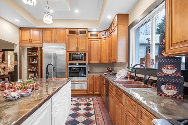 kitchen featuring black appliances, decorative light fixtures, dark stone countertops, sink, and a raised ceiling