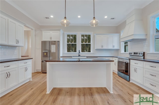 kitchen with appliances with stainless steel finishes, pendant lighting, backsplash, and light hardwood / wood-style floors