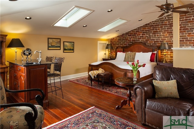 bedroom with dark hardwood / wood-style floors, ceiling fan, lofted ceiling with skylight, and brick wall