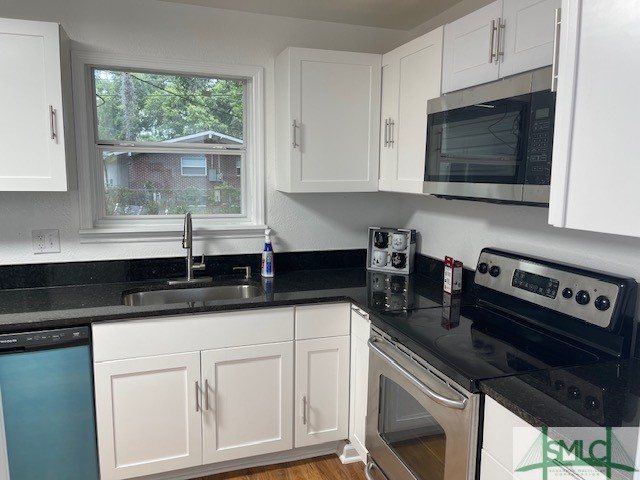 kitchen with white cabinetry, light hardwood / wood-style floors, sink, stainless steel appliances, and dark stone countertops