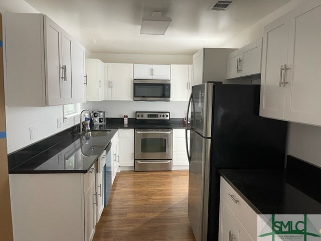 kitchen with appliances with stainless steel finishes, sink, dark wood-type flooring, and white cabinetry