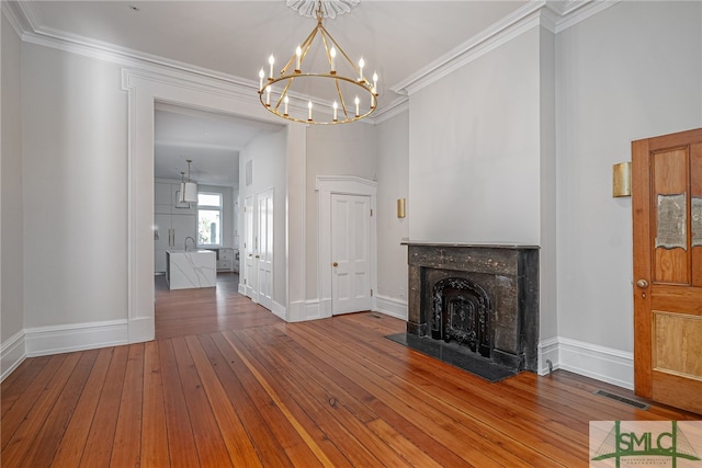 unfurnished living room with hardwood / wood-style flooring, a notable chandelier, ornamental molding, and a high end fireplace